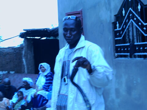 Un homme en boubou clair tenant une canne, lunettes relevées