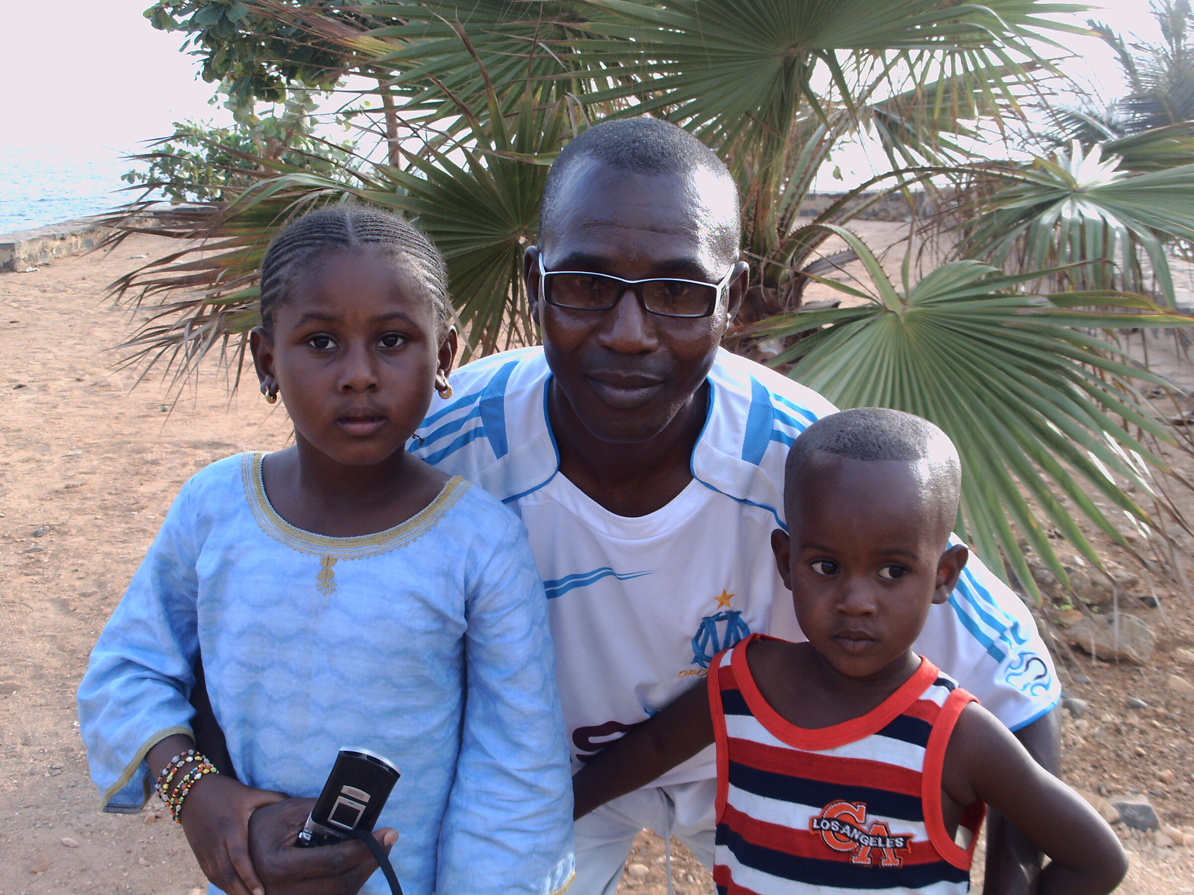 Un homme, une fillette et un jeune enfant devant des palmiers