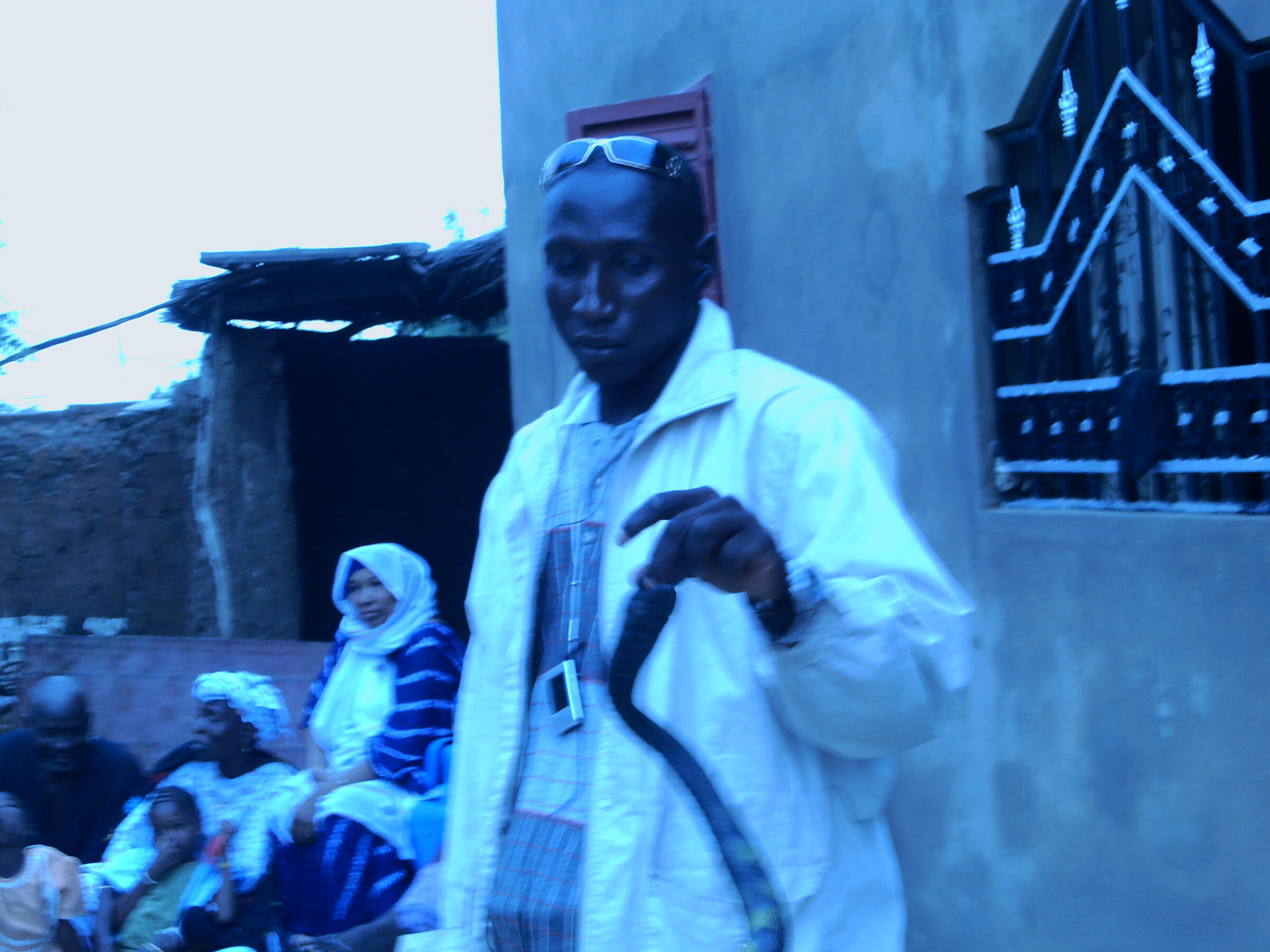 Un homme en boubou clair tenant une canne, lunettes relevées